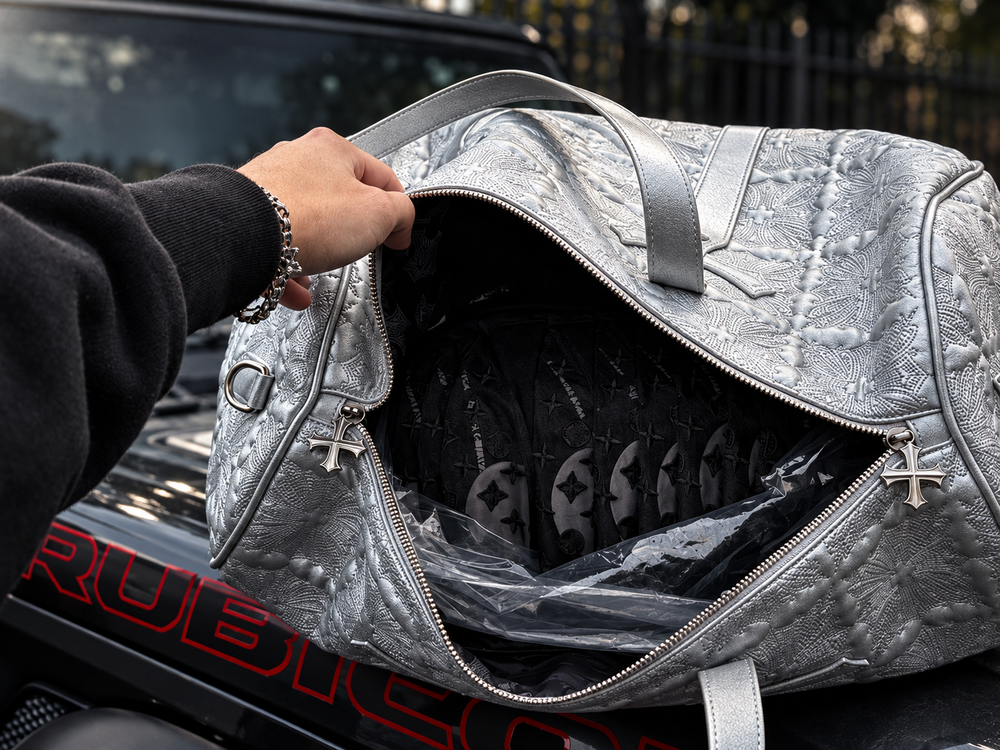 Dramatically lit silver duffel bag holding black clothing on a black Jeep.
